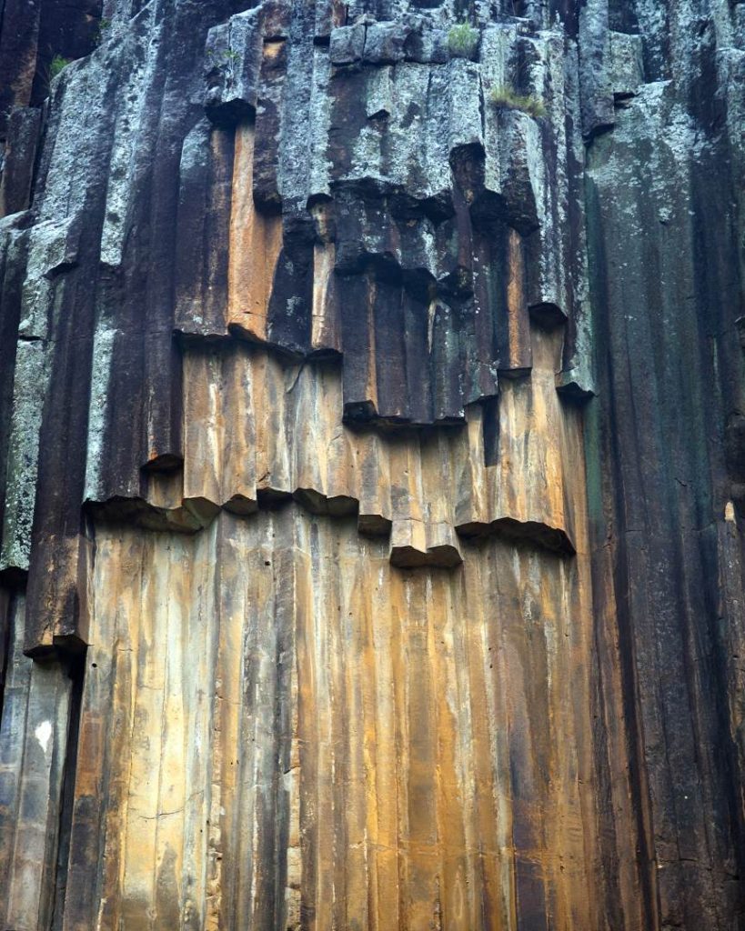Sawn Rocks, NSW, Columnar Basalt. Close-up of striking columnar basalt formations at Sawn Rocks, with hexagonal columns stacked like pillars. The natural rock formations are dark with orange-brown highlights, creating a unique geometric pattern in the landscape.