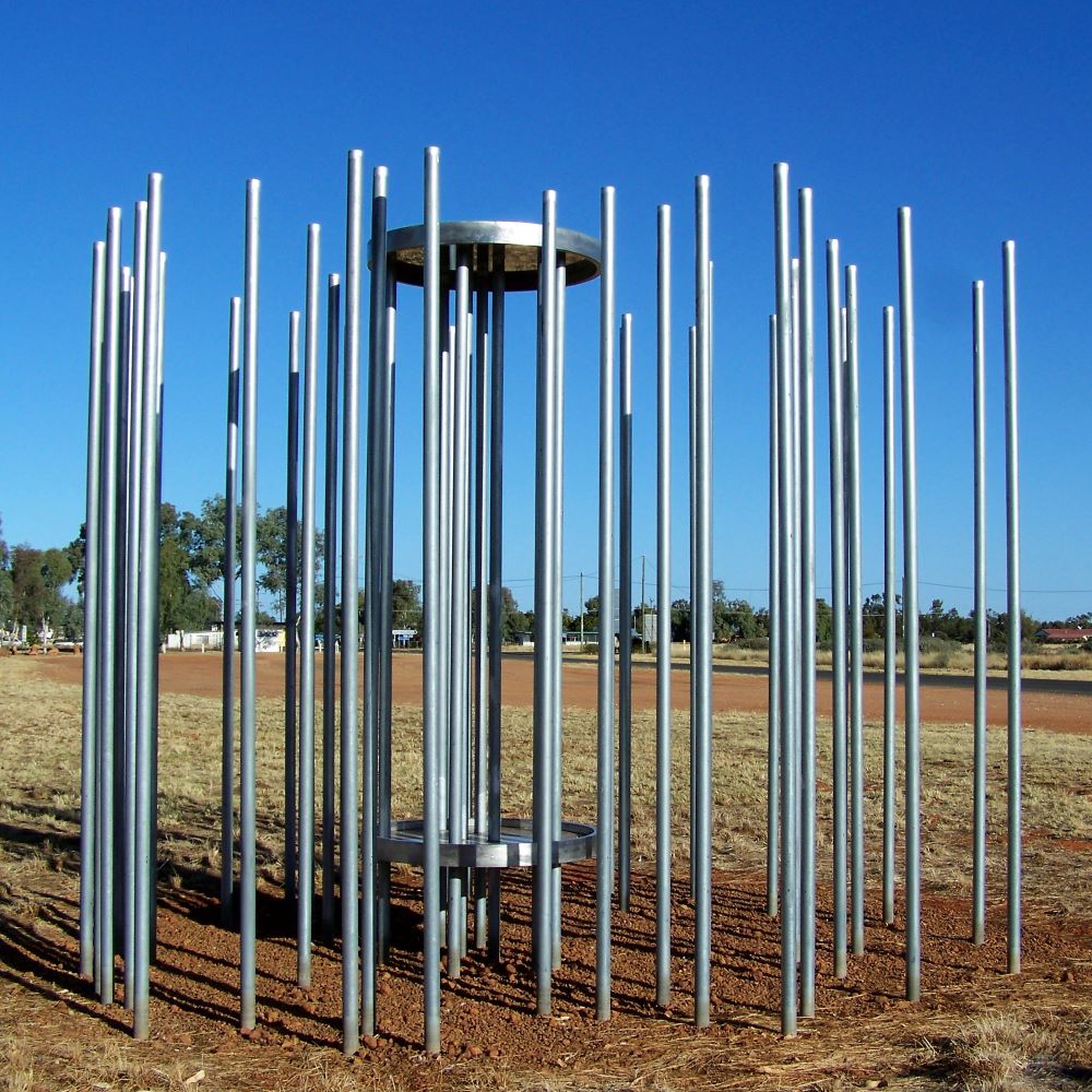 A sculpture titled "Conduit Between Above and Below" in Thargomindah, featuring vertical metal rods against a clear blue sky, representing one of the artistic attractions in the area.