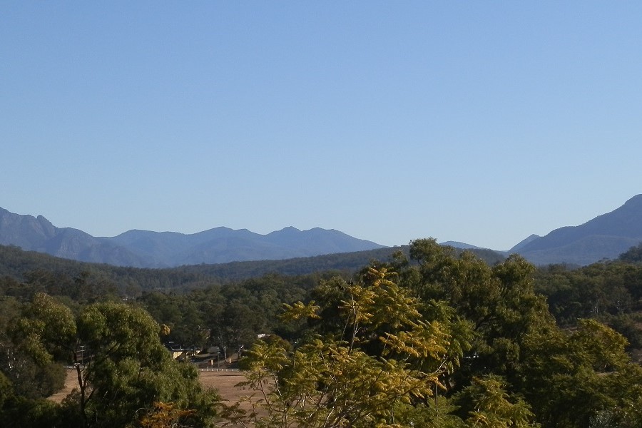 A scenic view from Rathdowney, showcasing tree-covered hills and distant mountain ranges under a clear blue sky.