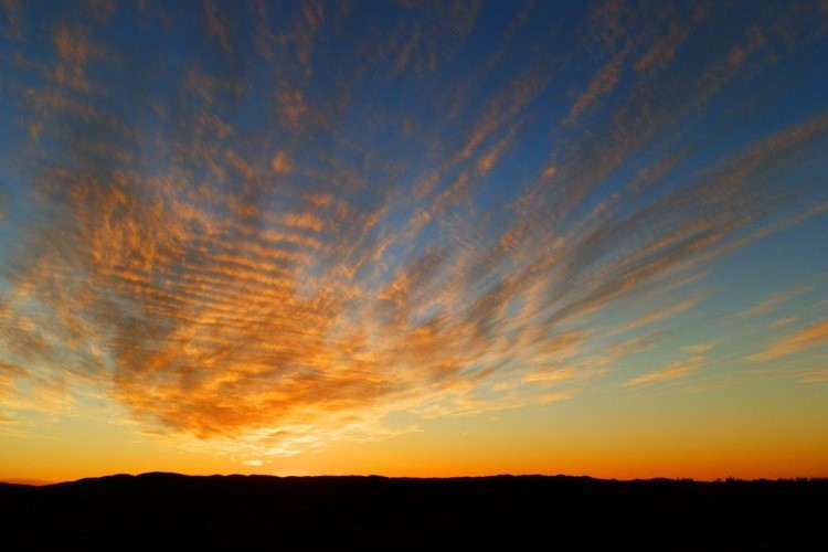 A vibrant sunset over Copley, with streaks of orange and gold clouds fanning out across the sky, creating a dramatic outback scene.
