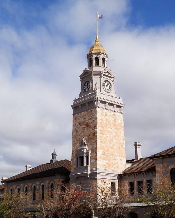 The historic clock tower in Kalgoorlie, Western Australia, stands tall with its golden dome and stone facade, set against a partly cloudy sky.