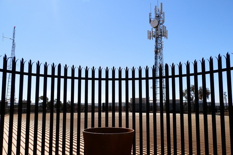 A fenced area at Mt Charlotte Reservoir in Kalgoorlie, Western Australia, with communication towers rising in the background against a clear blue sky.