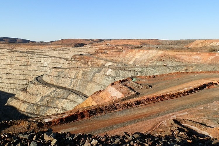 A section of the Super Pit in Kalgoorlie, Western Australia, shows terraced layers of the open-pit mine with winding roads cutting through the reddish and gray rock formations under a clear sky.