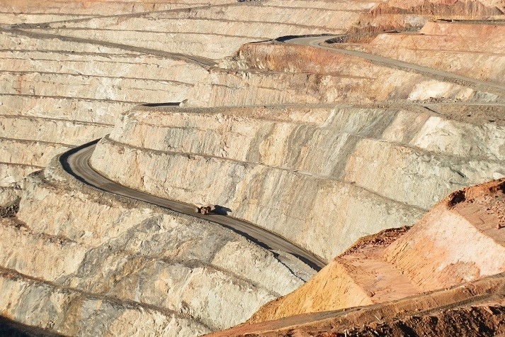 A large mining truck navigates a winding road along the terraced walls of the Super Pit in Kalgoorlie, Western Australia, emphasizing the vast scale of the open-pit mine.