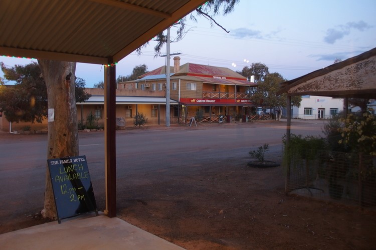 A view from a covered porch looking across the street at two pubs in Tibooburra, NSW. The scene is set at dusk with the soft evening light.