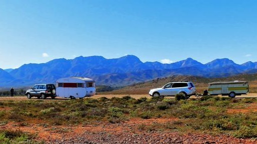 Caravans and trailers parked along a road with the dramatic Flinders Ranges in the background, near Wilpena Pound, South Australia.