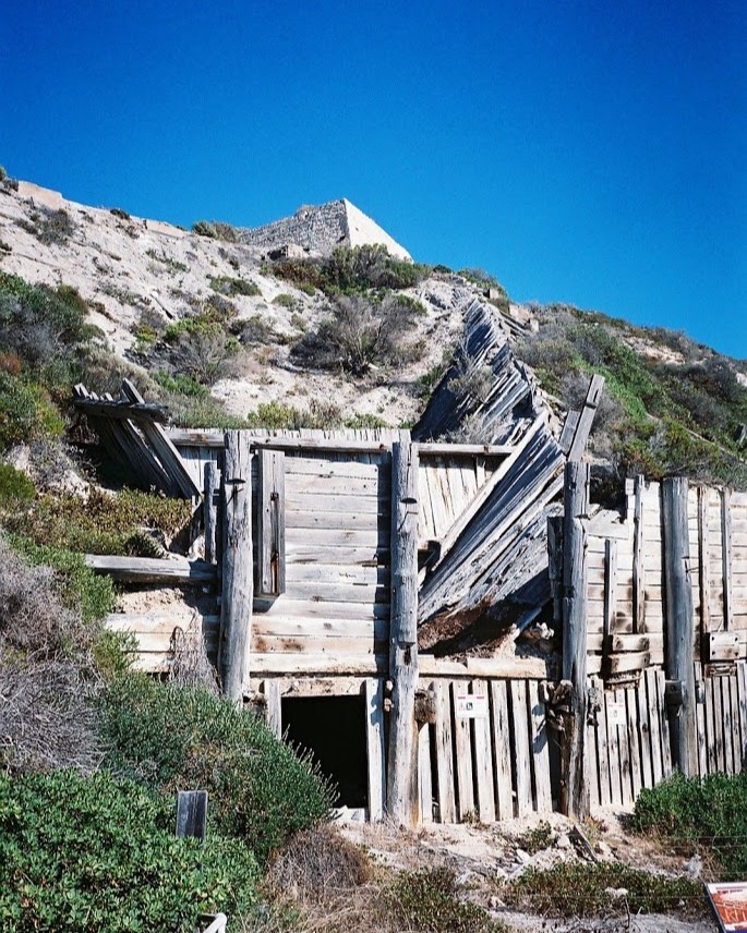 "The weathered wooden remnants of the Old Gypsum Mine set against a rocky hill in Dhilba Guuranda-Innes National Park, South Australia, showcasing the area's mining history.