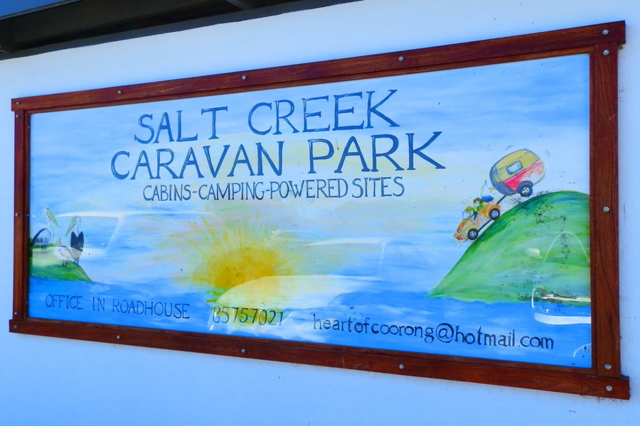 Sign for Salt Creek Caravan Park, advertising cabins, camping, and powered sites, with a colorful illustration of a camper and a sunrise, along with contact information for bookings. Sadly the caravan park closed in 2019.