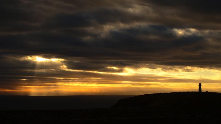 A moody sunset behind West Cape Lighthouse at Dhilba Guuranda-Innes National Park, Yorke Peninsula, South Australia, with golden light piercing through dark clouds