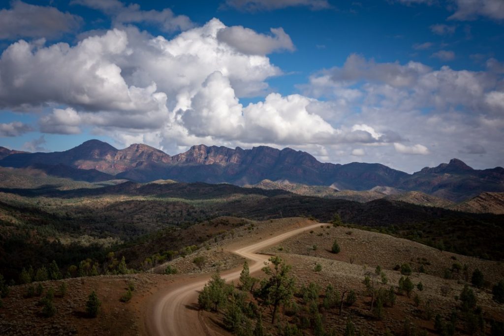 A dirt road winding through the Flinders Ranges under dramatic cloud cover, leading towards Wilpena Pound, South Australia.
