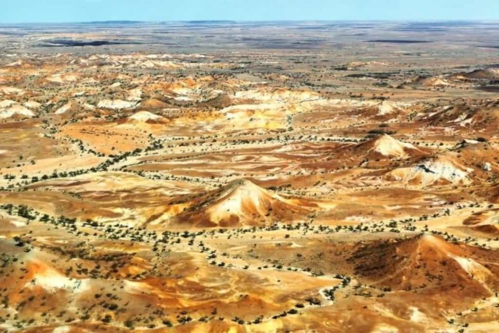 Aerial view of the Anna Creek Painted Hills in the outback of South Australia, featuring colourful mounds and rolling terrain with shades of red, orange, and white across the arid landscape.