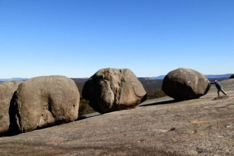 A man pushes a large boulder on a rocky hill in Bald Rock National Park, New South Wales, Australia.