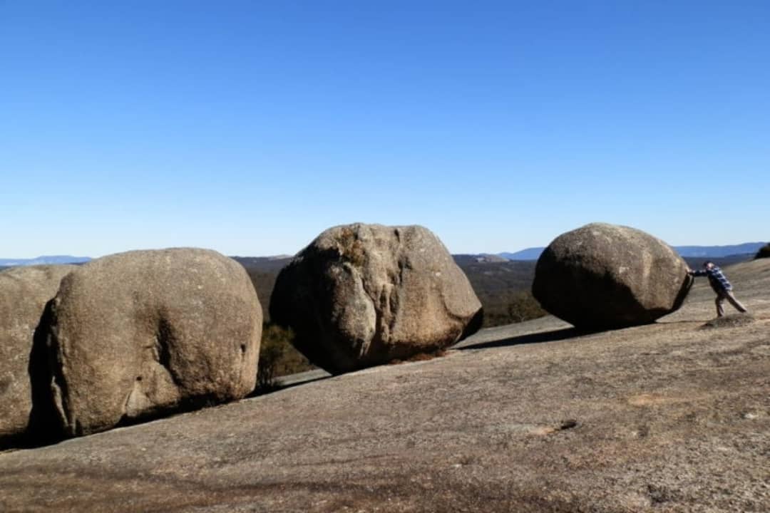 A man pushes a large boulder on a rocky hill in Bald Rock National Park, New South Wales, Australia.