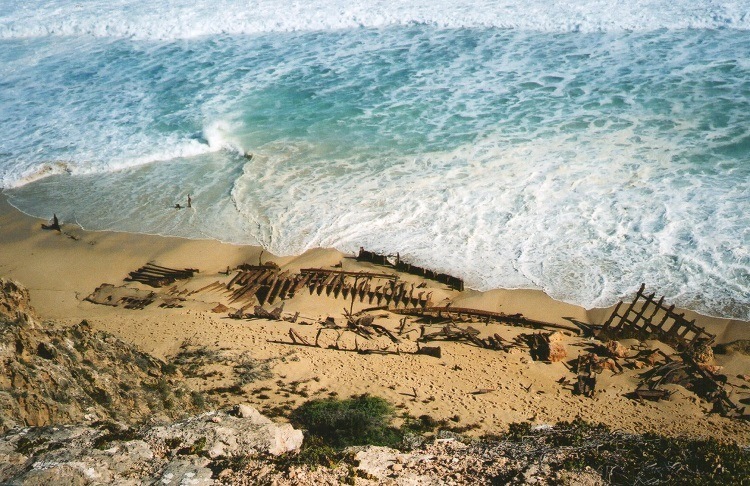 An overhead view of the Ethel Wreck remains scattered along the sandy beach at Dhilba Guuranda-Innes National Park, Yorke Peninsula, South Australia, with waves crashing onto the shore.