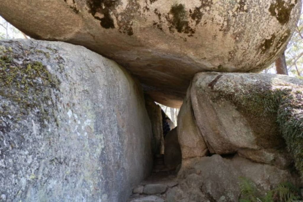 A narrow pathway leads under a large granite boulder that is precariously balanced on top of another boulder. This is a popular spot on the Bald Rock climb in Bald Rock National Park, New South Wales, Australia.