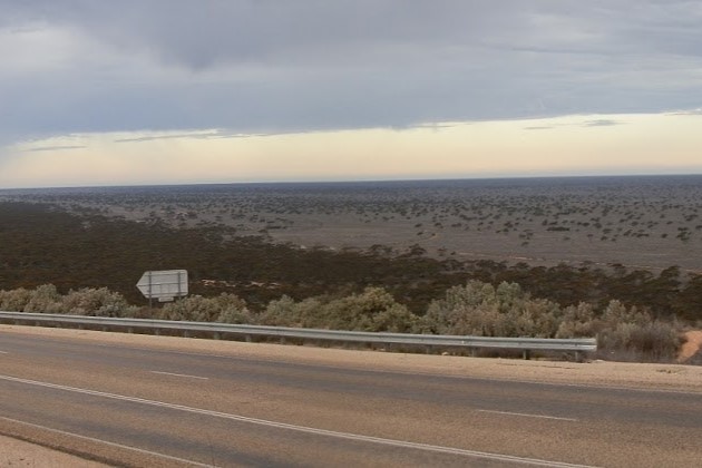 View from Madura Pass overlooking the vast, shrub-dotted expanse of the Nullarbor Plain under a cloudy sky.