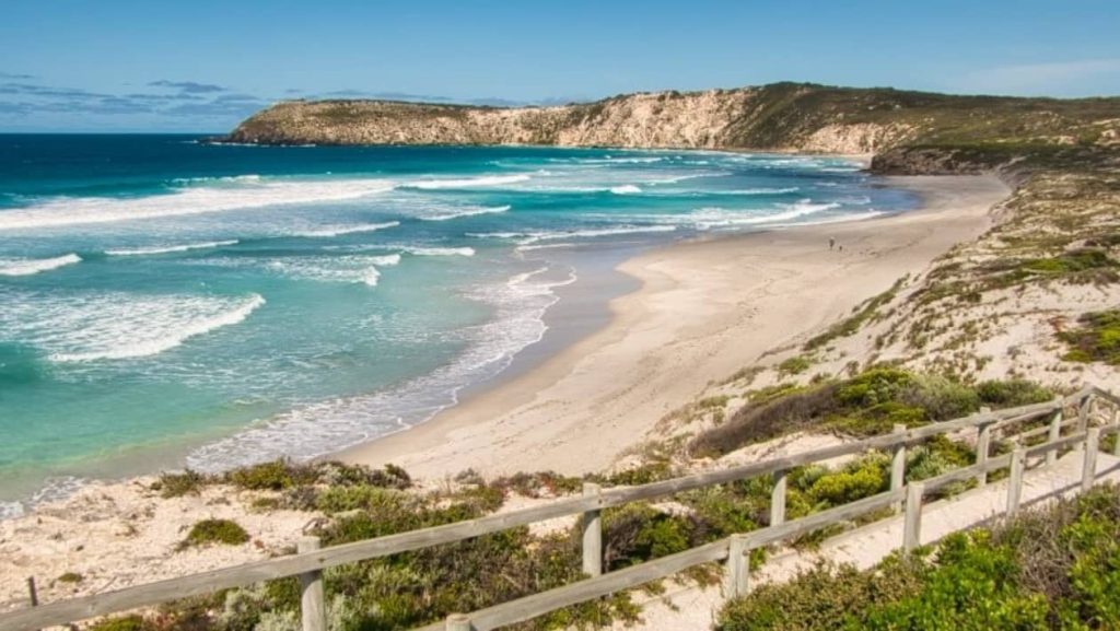 Scenic view of Pennington Bay on Kangaroo Island, South Australia, with turquoise waves crashing on the sandy shore, surrounded by cliffs and greenery.
