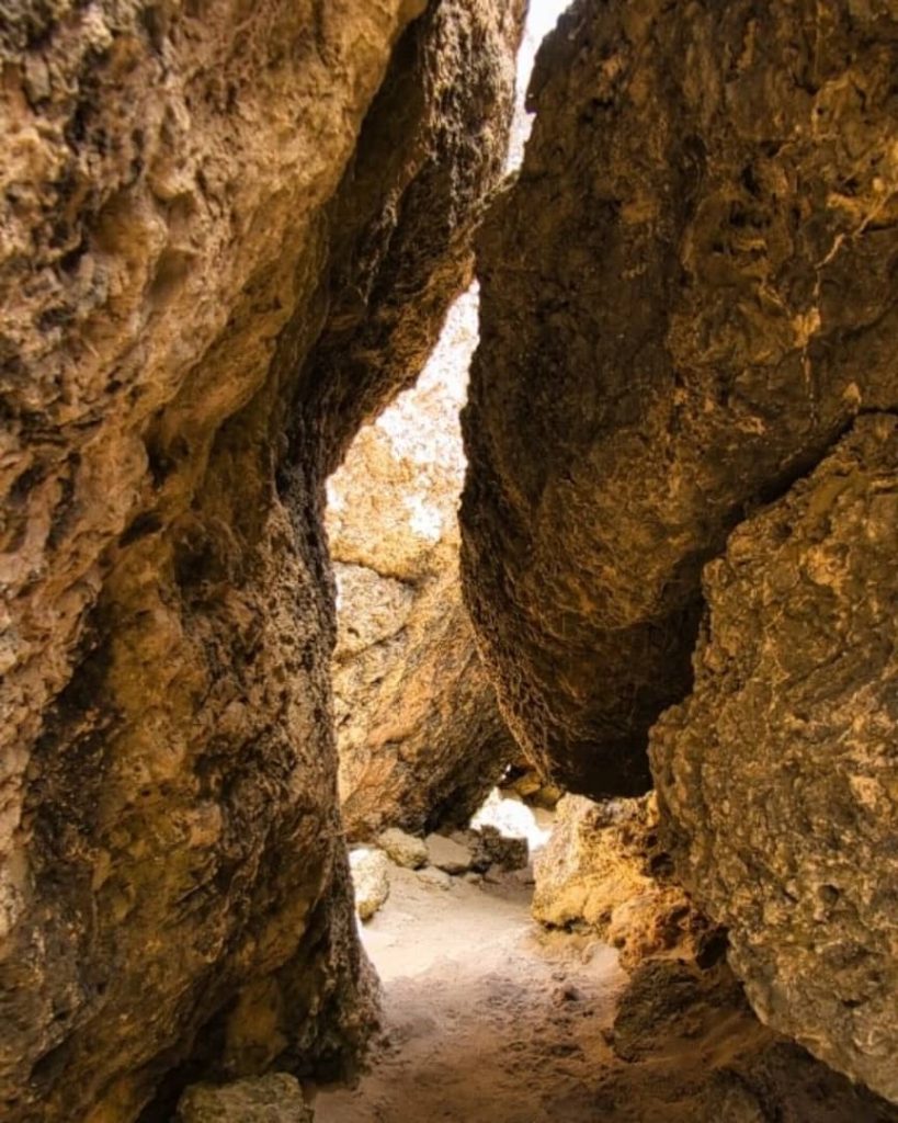 Narrow, rugged pathway through large rock formations leading to Stokes Bay, Kangaroo Island, with light filtering through the gaps.