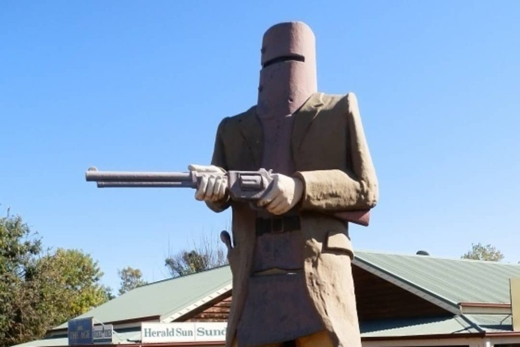 A large statue of a man wearing a helmet and holding a gun stands in front of a building. A woman stands in front of the statue, looking up at it.