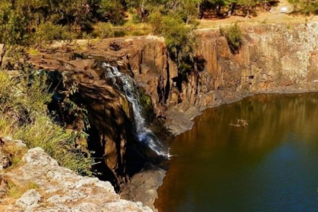 A scenic view of Tooloom Falls with water cascading down a rocky cliff into a natural pool, surrounded by greenery near Woodenbong.