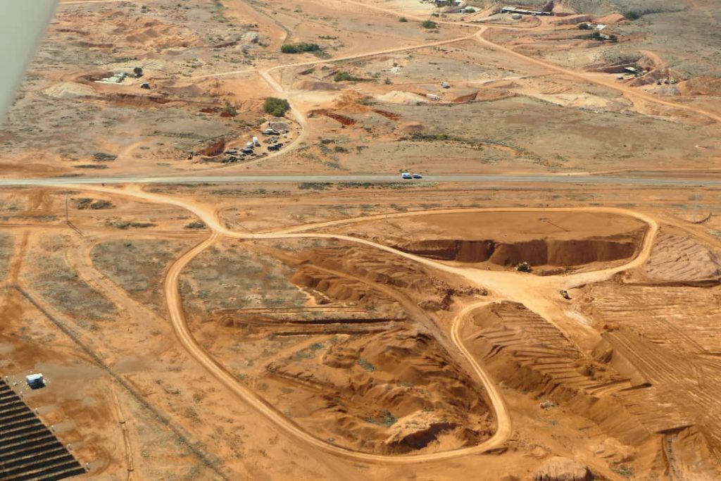 Aerial view of mining sites in Coober Pedy, South Australia, showing excavated areas, dirt roads, and sparse desert terrain.