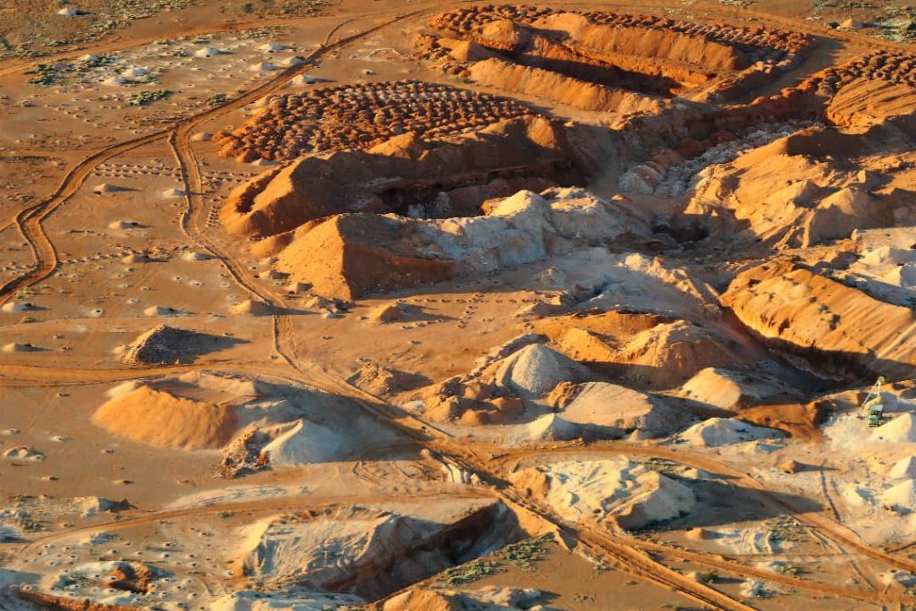 Aerial view of opal mines in Coober Pedy, South Australia, showcasing rugged, dusty terrain with multiple mine shafts and mounds of excavated earth.