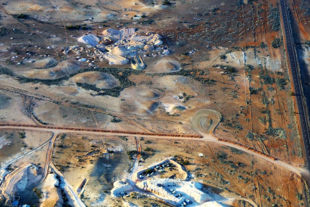 Aerial view of Coober Pedy’s opal mines in the early morning light, showing scattered mine shafts and dirt roads across the arid outback landscape in South Australia.