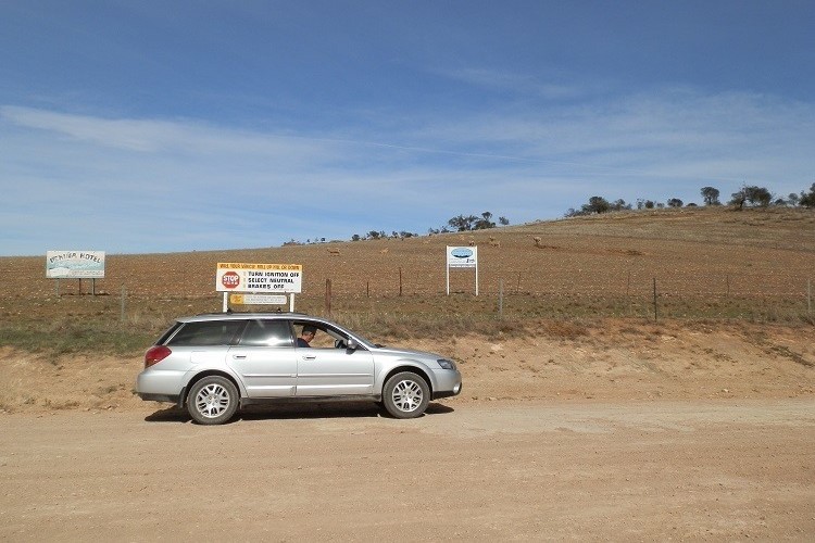 A silver car parked near signs on a dirt road at Magnetic Hill, South Australia.