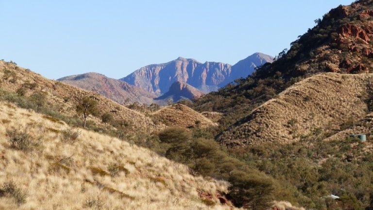 Mt Sonder, a must-see for things to do in Central Australia, with rugged peaks and rolling grassy hills under a clear blue sky.