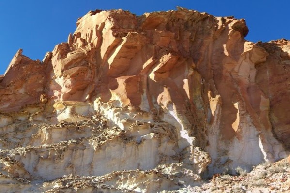Colorful sandstone cliffs at Rainbow Valley, a striking geological feature and a must-see when looking for things to do in Central Australia. The vibrant red, orange, and white layers stand out against the clear blue sky.