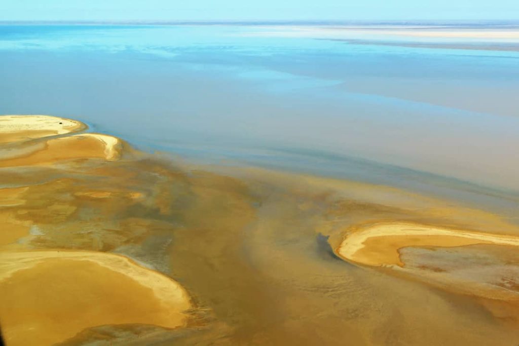 Aerial view of sandbars surrounded by saltwater on Lake Eyre, highlighting the contrasting colours and serene patterns in the South Australian outback.