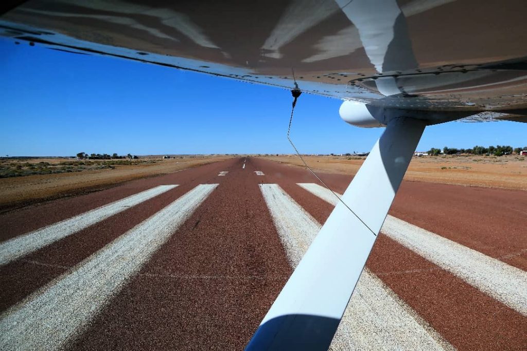 iew from an aircraft preparing for takeoff from the William Creek airstrip in South Australia, showing the red dirt runway stretching into the outback under a clear blue sky.