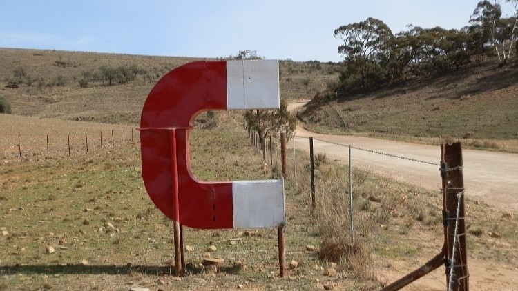 A large red and white magnet sculpture at Magnetic Hill, South Australia, by a rural dirt road.