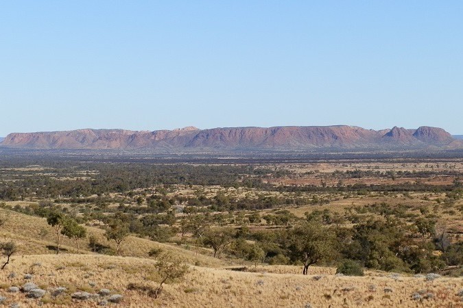 Distant view of Tnorala (Gosse Bluff) from Tylers Pass Lookout, a scenic stop for things to do in Central Australia, with red ridges and vast plains under clear skies.