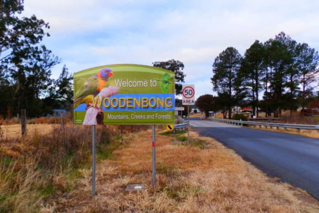 Welcome sign at the entrance of Woodenbong, NSW, featuring vibrant imagery of a parrot and text highlighting the area's mountains, creeks, and forests.