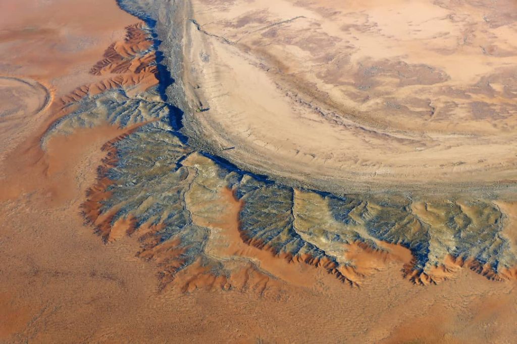 Aerial view of dried riverbeds and eroded land formations in the outback of South Australia, displaying a mix of earthy tones and rugged textures.
