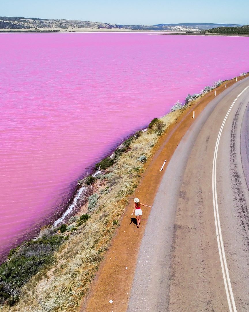 A person walking along a road next to the strikingly vibrant Pink Lake in Kalbarri.