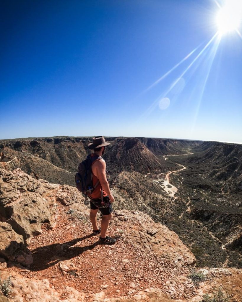 A hiker standing at the edge of Shothole Canyon, overlooking the dramatic red rock landscape.