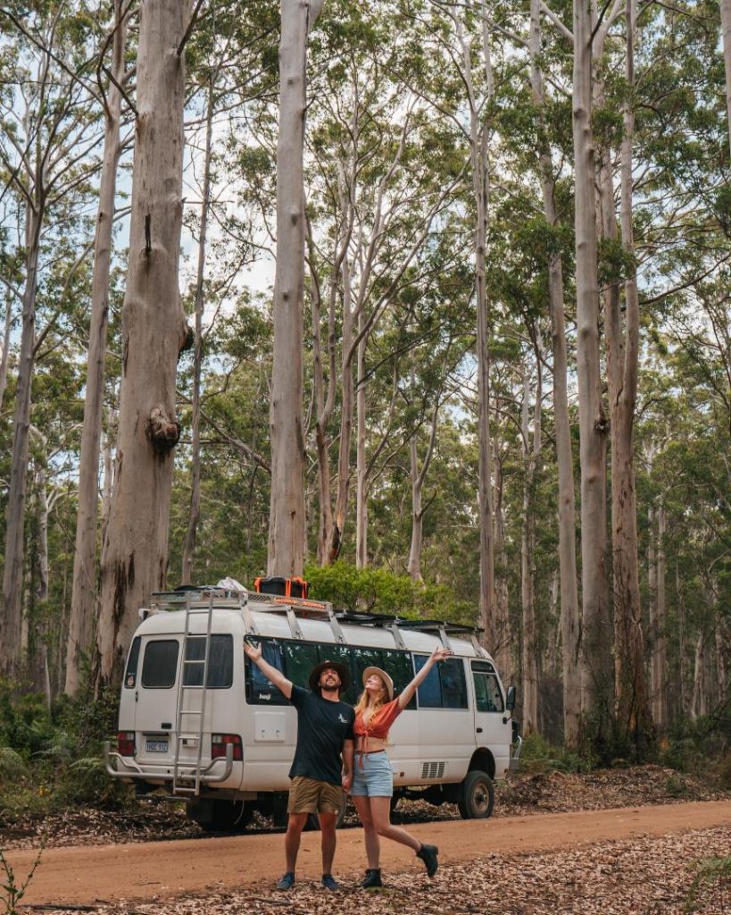 A couple standing beside their campervan surrounded by tall trees in Boranup Forest, Margaret River.