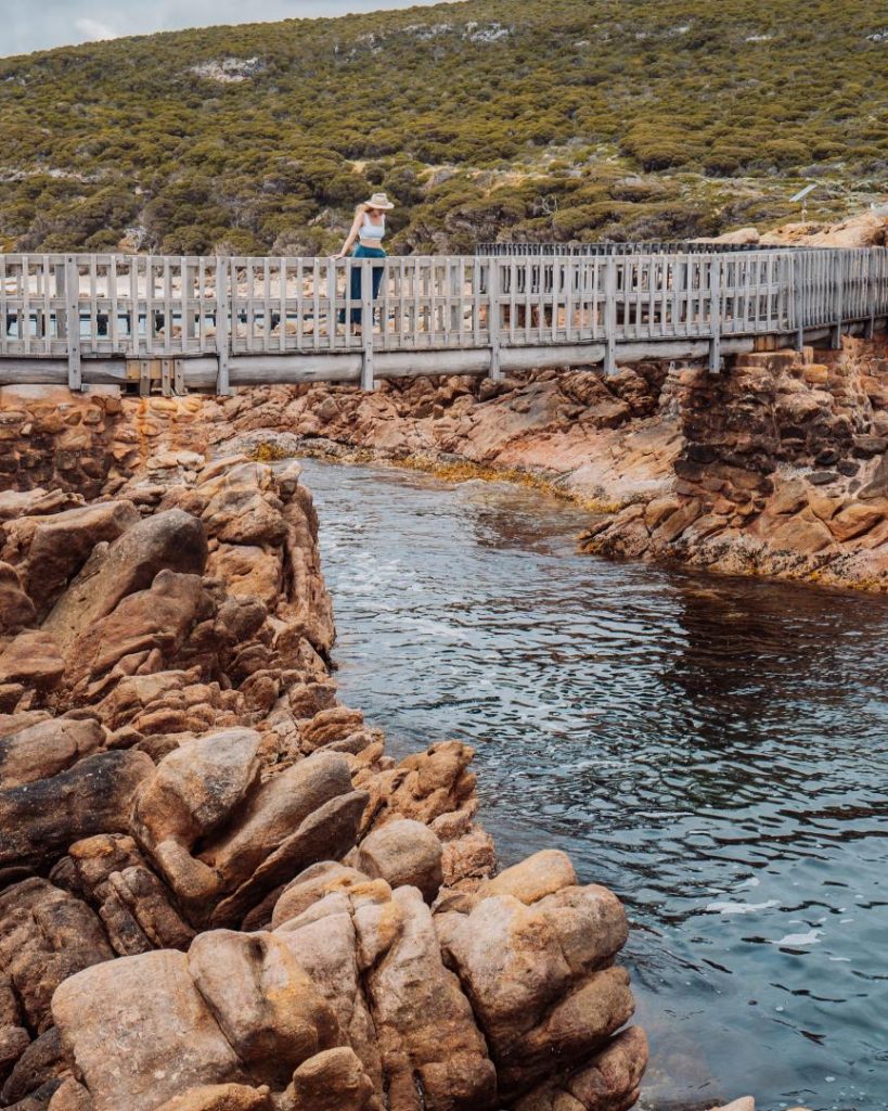 A person standing on a wooden bridge with rugged rocks and flowing water below at Canal Rocks.