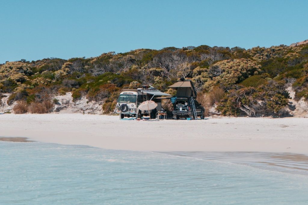 A camper van and a 4WD with a rooftop tent parked on Wharton Beach, surrounded by untouched white sand and coastal scrub