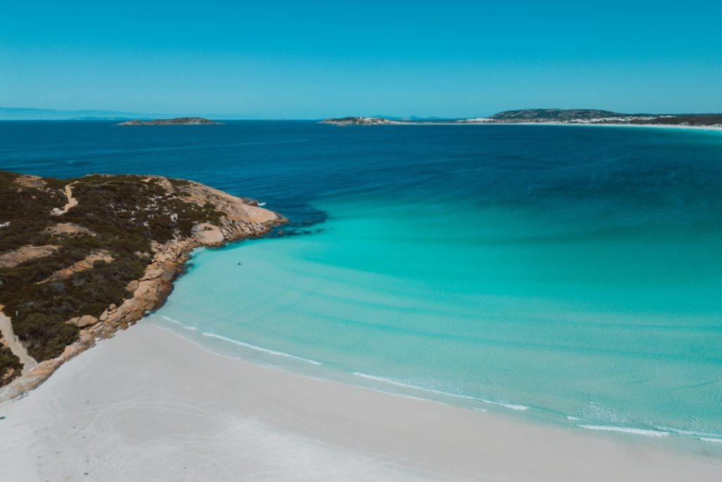 A stunning aerial view of Wharton Beach, featuring crystal-clear turquoise waters and pristine white sand surrounded by rugged coastal greenery.
