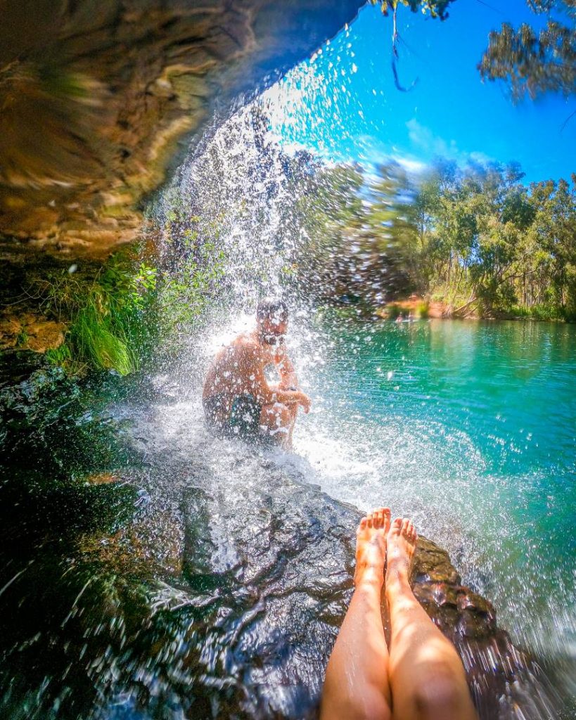 A lush green waterfall cascading into the crystal-clear waters of Fern Pool, framed by vibrant vegetation.