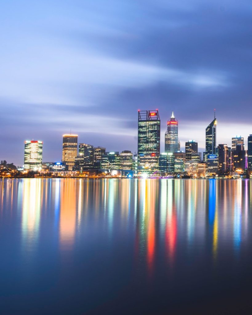 A vibrant night view of Perth’s illuminated skyline reflecting across the still water.