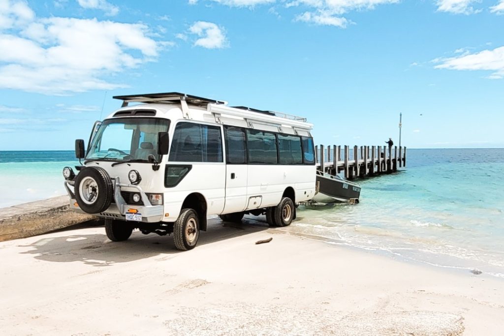 A rugged, white vehicle with a boat trailer is parked on the beach near Busselton Jetty’s boat ramp, set against the backdrop of turquoise waters. This image reflects the jetty's accessibility for boating and marine activities in Western Australia.