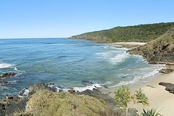 A scenic view of the secluded beach at Broken Head Coastal Reserve, with rocky cliffs, sandy shores, and lush greenery, showcasing a hidden gem among the things to do in Ballina NSW for beach lovers and adventurers.