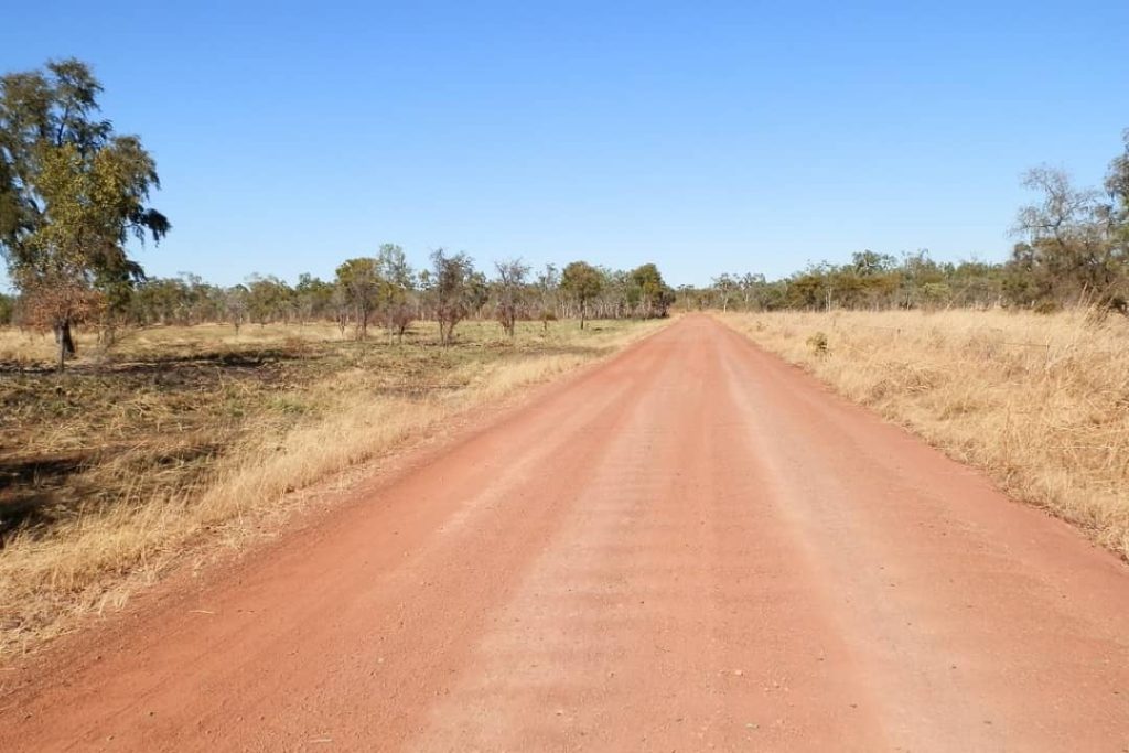 A long, red dirt road stretching through dry grasslands and sparse trees in Gregory National Park, near Timber Creek in the Northern Territory.