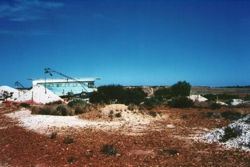 An old bus converted into a home set against the backdrop of the White Cliffs opal fields in New South Wales, with mounds of excavated earth nearby.