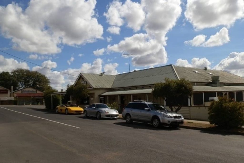 Vintage cars parked outside heritage building in Aratula township, with cloudy blue sky above.