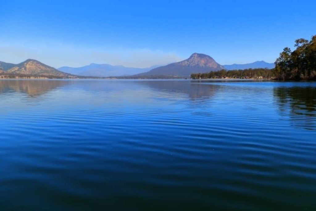 View of Lake Moogerah with gentle ripples and a distant smoke haze over the mountains of the Scenic Rim, Queensland.